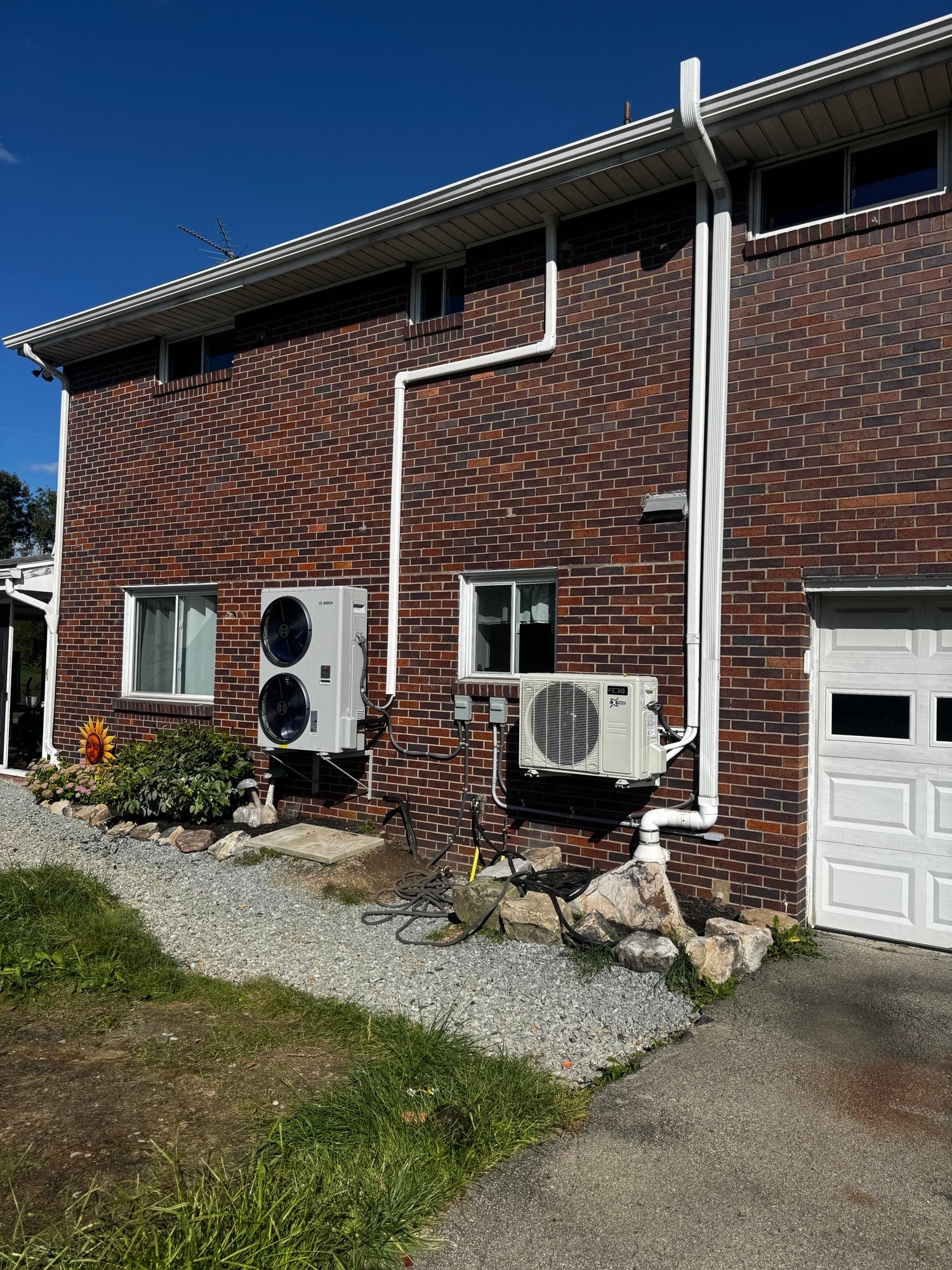 Wide exterior view of completed Bosch IDS Edge heat pump installation on brick home in Liberty, PA — line-hide runs and both outdoor units visible
